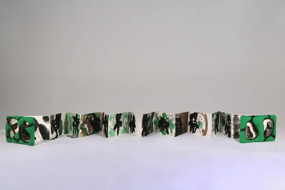 The accordion artbook fully extended, green padded covers at each end