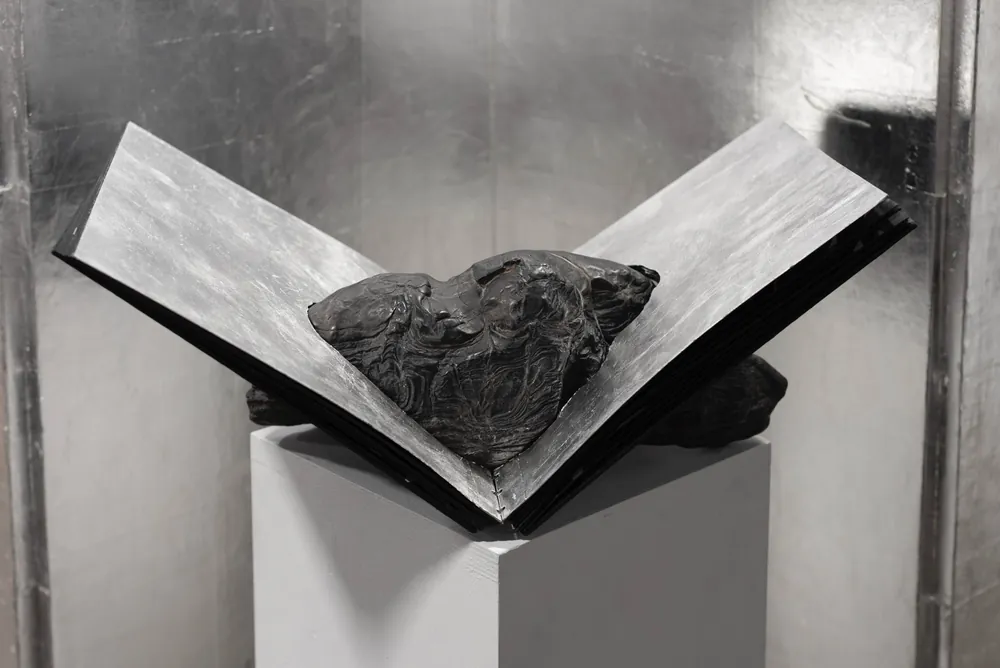 A dark stone resting on an open, book-like form on a plinth
