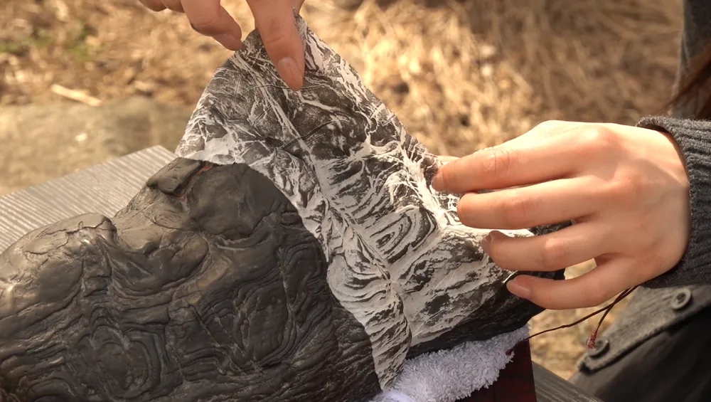 Hands lifting a freshly taken rubbing from a stone outdoors